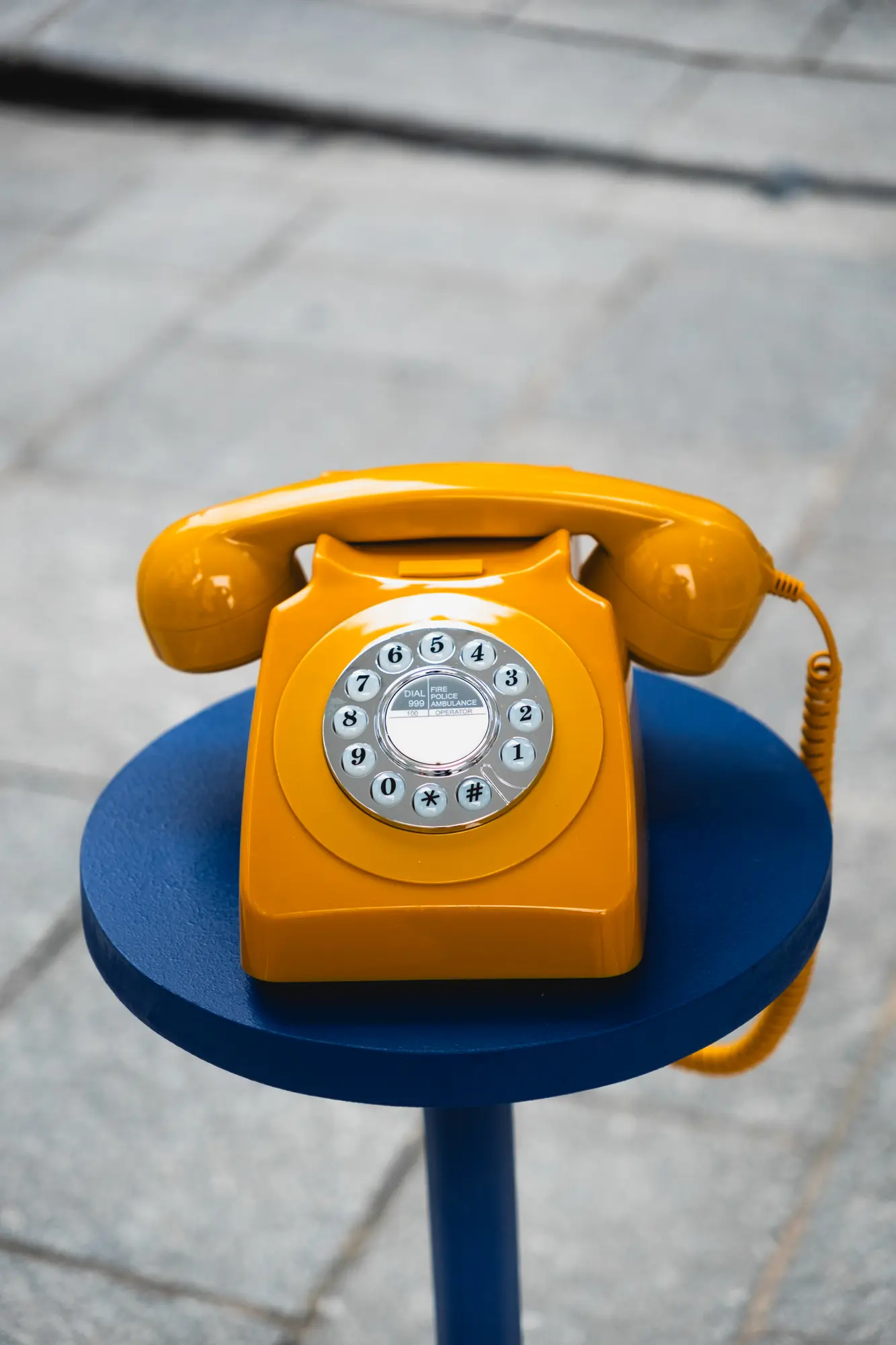 Téléphone à cadran jaune posé sur son socle bleu dans la cabine